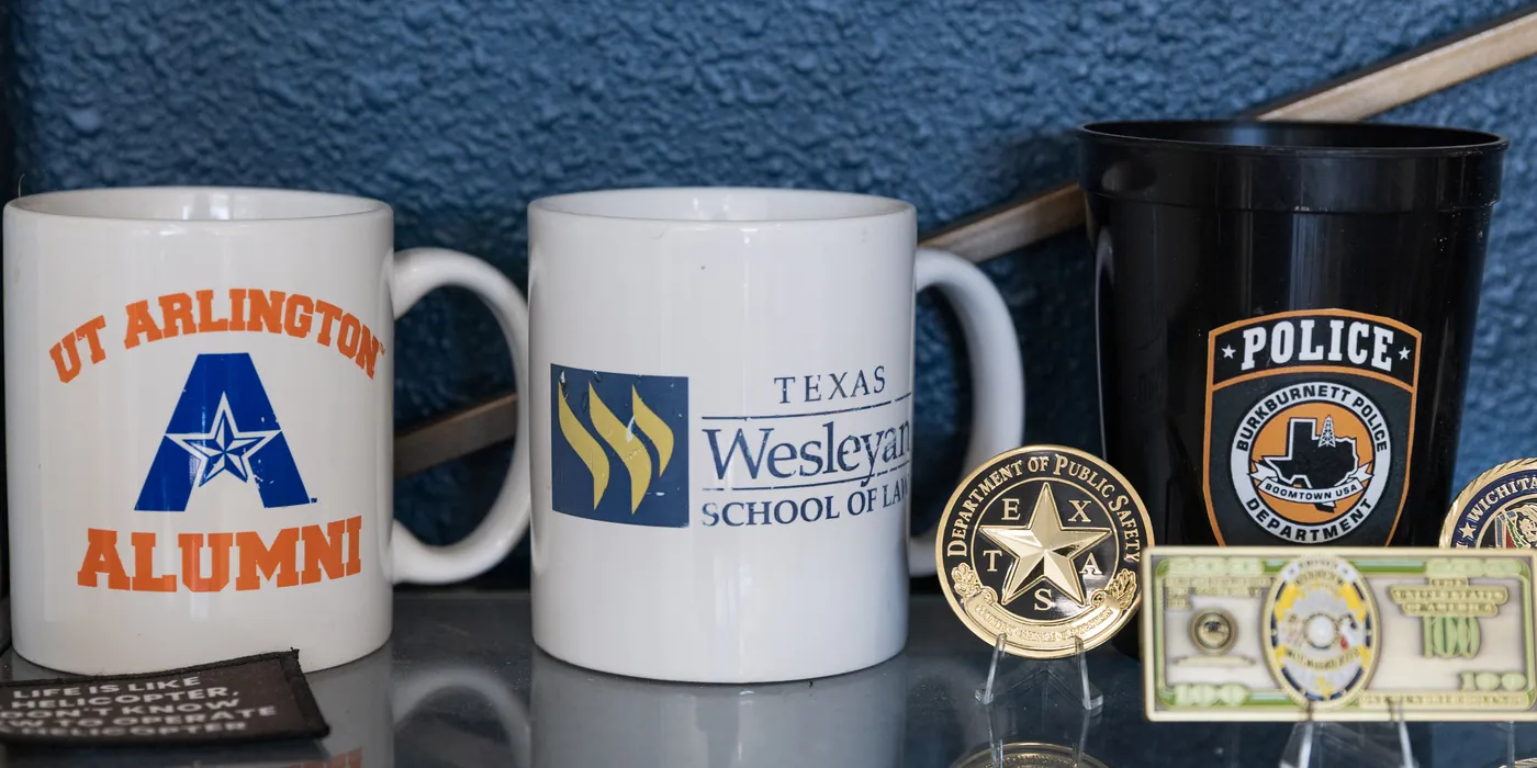 Mugs from The University of Texas at Arlington and Texas Wesleyan School of Law on Joe's desk